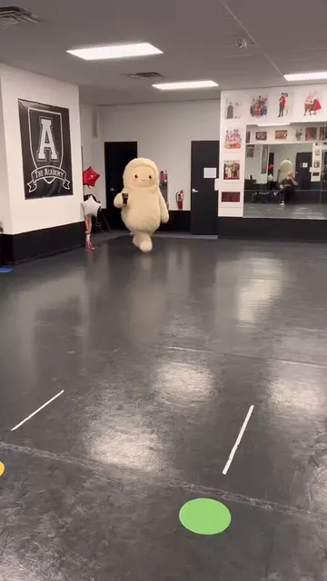 Muse, a fluffy character, hopping on one foot in a dance studio